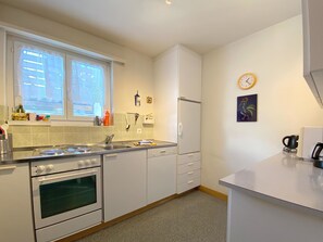 Ett modernt kök med vita skåp, en spis, en ugn, ett diskho och ett fönster med dekorativa gardiner.