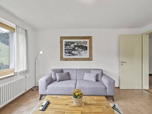 Ein Wohnzimmer mit grauem Sofa, einem gerahmten Schwarz-Weiß-Foto an der Wand, einer Stehlampe, einer Fernbedienung und einem Blumenkorb auf einem Holztisch.
