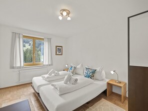A hotel room with two beds, a window with curtains, a radiator, a framed picture on the wall, and a nightstand with a lamp. - Bellavista 6 Appartement/Fewo, Bad, WC, 3 Schlafräume Ferienwohnung Bellavista 6 by Interhome (Parpan)