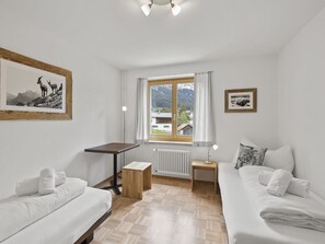 Ein Zimmer mit zwei Betten, einem Tisch, einem Heizkörper und einem Fenster mit Bergblick.