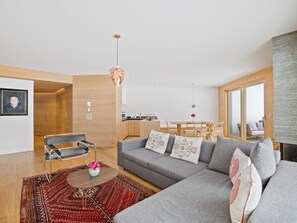 A modern living room with a grey sofa, a wooden dining table, and a red patterned rug. - Praval Appartement/Fewo Ferienwohnung Praval by Interhome (Valbella)