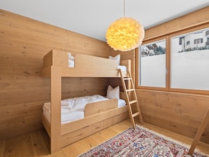 A bunk bed room with a wooden floor, a patterned rug, and a window with a view of a building. - Praval Appartement/Fewo Ferienwohnung Praval by Interhome (Valbella)