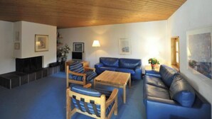 Un soggiorno arredato con soffitto in legno, un divano blu, un tavolino da caffè in legno e una televisione.