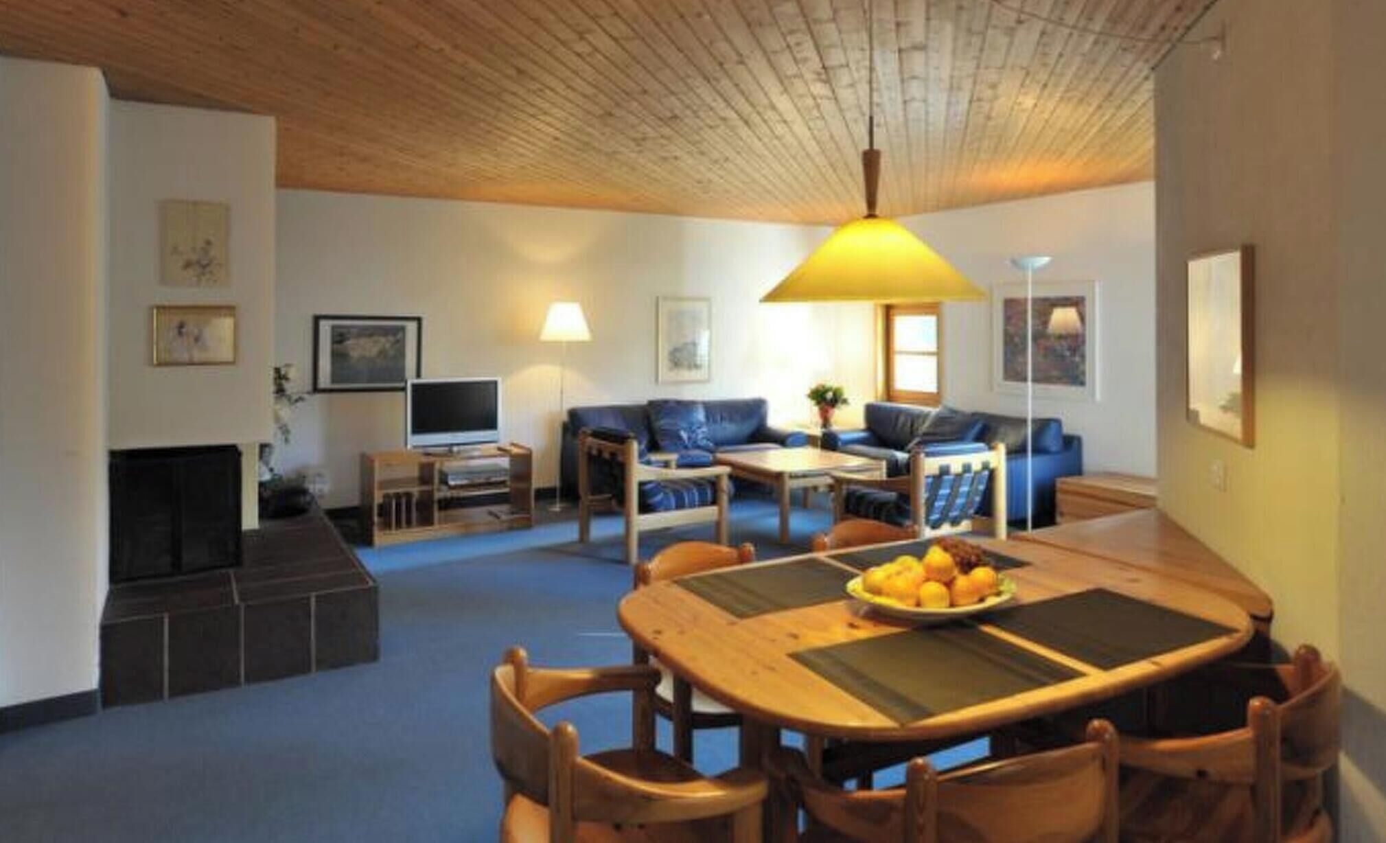A living room with a fireplace, a sofa set, a dining table with chairs, and a television.