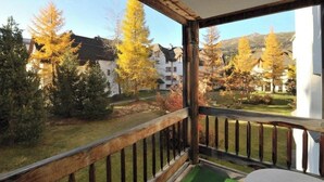 Un balcone con ringhiera in legno che si affaccia su un giardino con alberi e un edificio sullo sfondo.