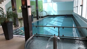 Una piscina interna con barriera in vetro, una vasca idromassaggio e una scala che conduce a un livello superiore.