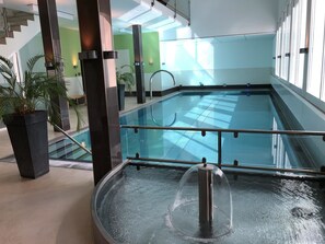 Ein Innenpool mit Glasbarriere, einem Whirlpool und einer Treppe, die zu einer erhöhten Ebene führt.