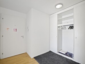 Ein Zimmer mit einer weißen Tür, einem grauen Teppich und einem weißen Kleiderschrank mit darin hängender Kleidung.