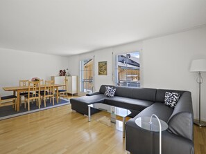 A modern living room with a sectional sofa, a glass coffee table, and a dining area with wooden furniture. - Moser Appartement/Fewo Ferienwohnung Moser by Interhome (Churwalden)
