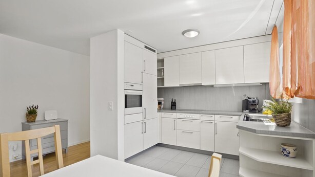 Et moderne køkken med hvide skabe, en indbygget ovn og et spiseområde med bord og stole.