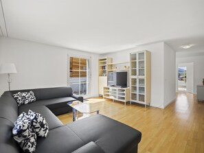 A modern living room with a grey sofa, a glass coffee table, and a TV stand with a flat-screen TV. - Moser Appartement/Fewo Ferienwohnung Moser by Interhome (Churwalden)