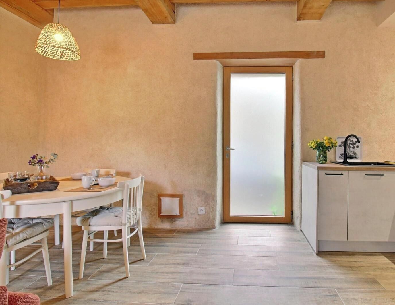 A kitchen with a wooden ceiling, a dining area with a table and chairs, and a sliding glass door leading to a balcony.