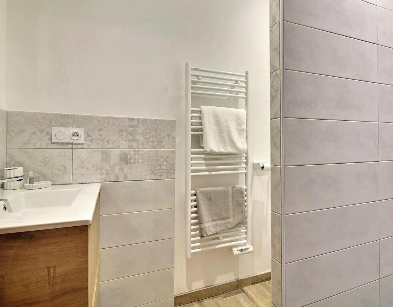 A modern bathroom with a white sink, a towel rack, and patterned tiles on the wall.