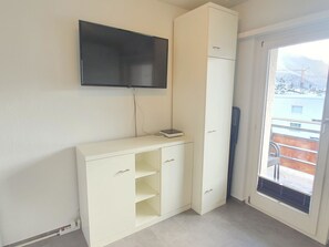 Ein Zimmer mit einem weißen Schrank, einem an der Wand befestigten Flachbildfernseher und einer Glastür zu einem Außenbereich.