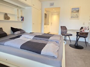 A modern bedroom with a large bed, a desk, and a chair. There is a small kitchenette in the corner. - Studio 406 Appartement/Fewo Studio 406 by Interhome (Lenzerheide)
