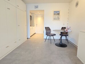 A compact kitchen with white cabinets, a dining area with two chairs and a small round table, and a hallway leading to another room. - Studio 406 Appartement/Fewo Studio 406 by Interhome (Lenzerheide)