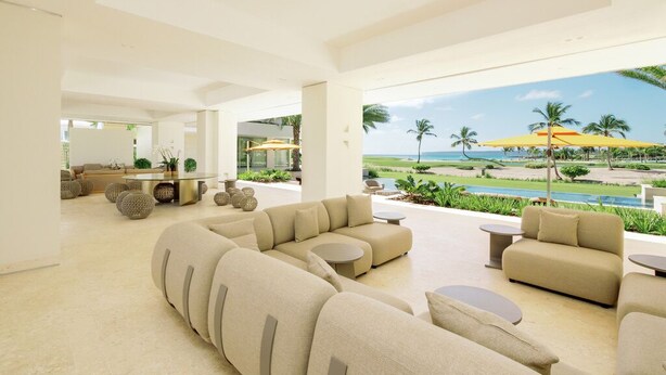 A spacious living area with a large sectional sofa, round coffee tables, and a view of a pool and palm trees. - Shemesh Residence - Ocean & golf views with full staff at unique Cap Cana villa (Cap Cana)