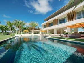 A modern pool area with clear water, outdoor seating, and a two-story building with large windows.