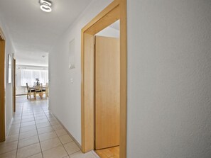 A hallway with a wooden door, white walls, and a tiled floor leading to a dining area with a table and chairs. - Ruggli Appartement/Fewo,   Ferienwohnung Ruggli by Interhome (Churwalden)