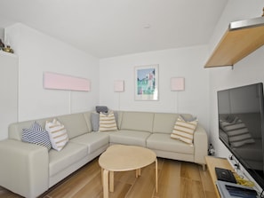 Ein modernes Wohnzimmer mit einem beigefarbenen Ecksofa, einem runden Couchtisch, einem Flachbildfernseher und einem Holzbalken an der Decke.