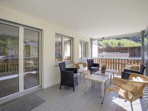 A modern outdoor patio with wicker furniture, a glass door leading to a balcony, and a view of a hilly landscape. - Ruggli Appartement/Fewo,   Ferienwohnung Ruggli by Interhome (Churwalden)