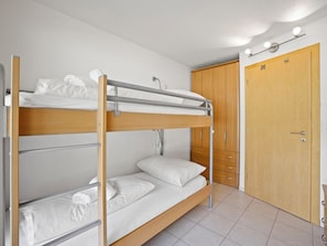 Ein Stockbett mit Holzrahmen und weißer Bettwäsche, ein Kleiderschrank mit mehreren Schubladen sowie eine Tür mit Griff.