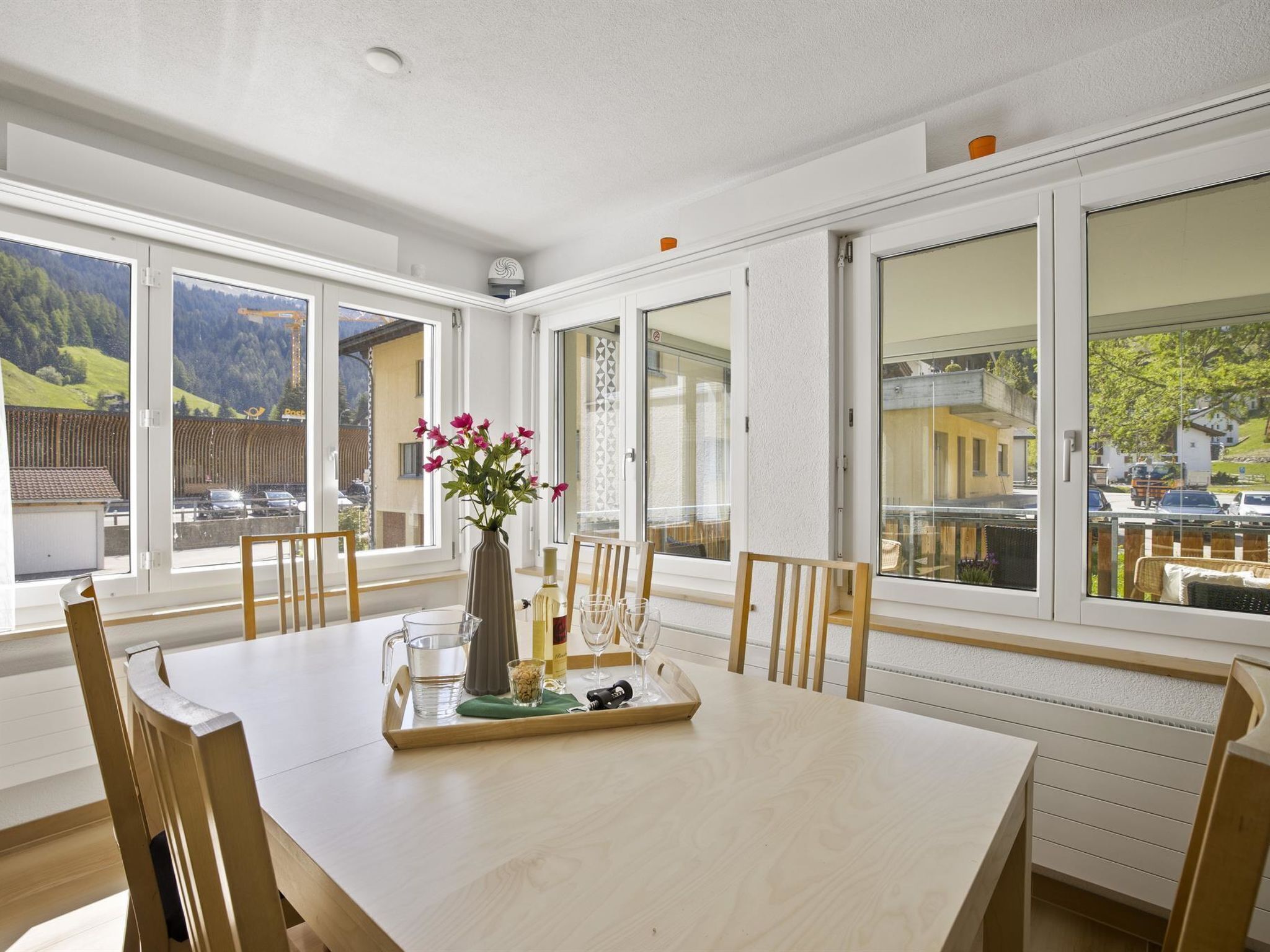 Ein Essbereich mit einem Tisch für zwei Personen, einer Blumenvase und Blick auf eine Berglandschaft durch große Fenster.
