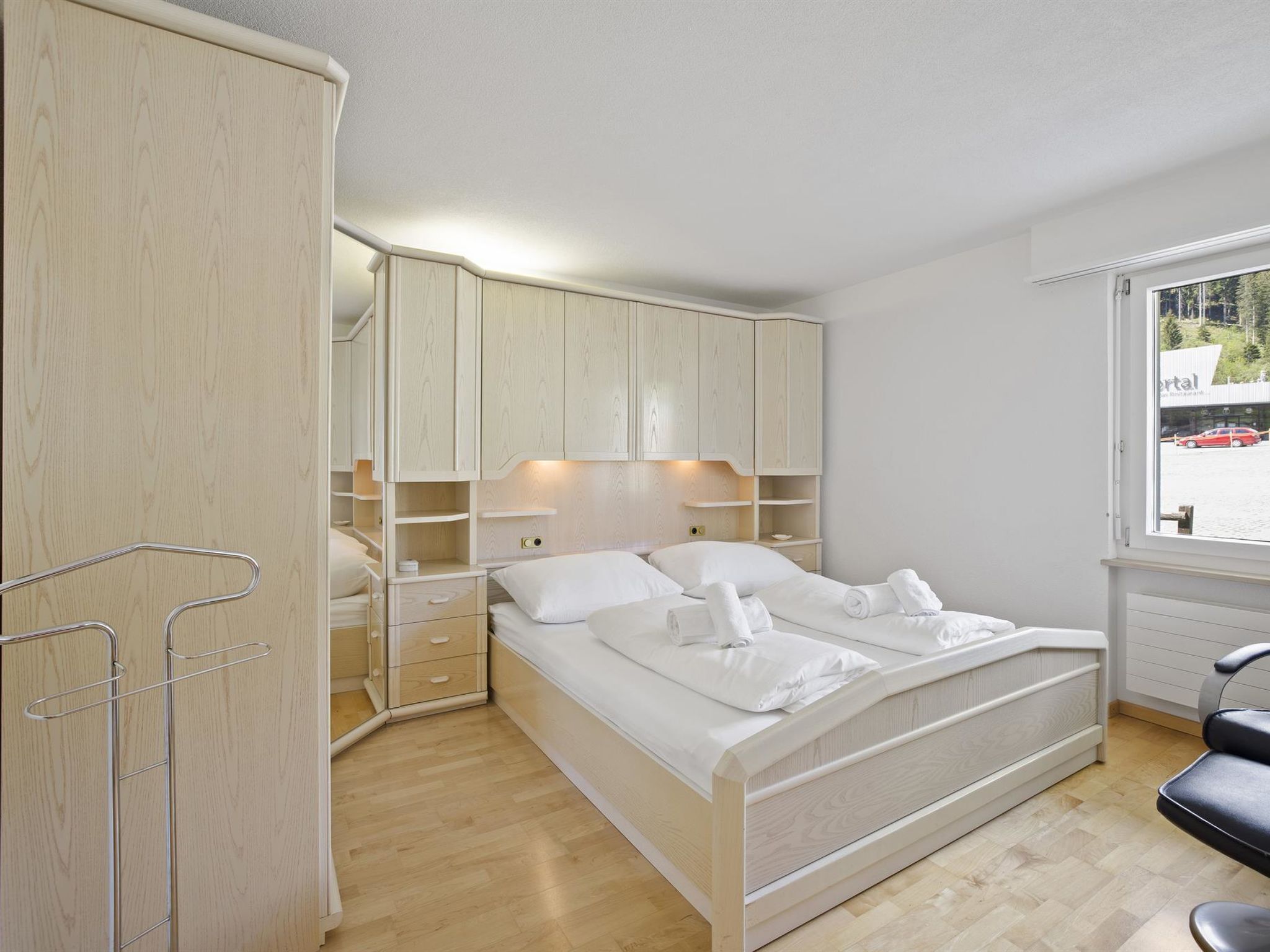 Une chambre à coucher avec un lit, une armoire en bois et une fenêtre donnant sur un bâtiment à l’extérieur.