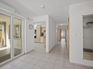 Ein modernes Interieur mit einem Flur, der in einen Küchenbereich führt, mit Schiebegläsern, einer sichtbaren Uhr und einem gefliesten Boden.