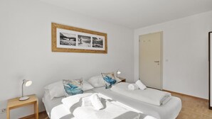 A bedroom with two beds, a bedside table with a lamp, a framed picture on the wall, and a door. - Bellavista 4 Appartement/Fewo, Bad, WC, 2 Schlafräume Ferienwohnung Bellavista 4 by Interhome (Parpan)