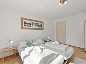 A bedroom with two beds, a bedside table with a lamp, a framed picture on the wall, and a door. - Bellavista 4 Appartement/Fewo, Bad, WC, 2 Schlafräume Ferienwohnung Bellavista 4 by Interhome (Parpan)