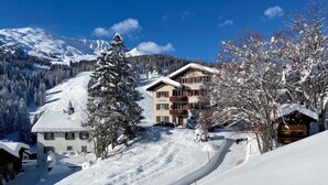 A snow-covered mountain resort with a multi-story building, ski slopes, and a clear blue sky. - Bellavista 4 Appartement/Fewo, Bad, WC, 2 Schlafräume Ferienwohnung Bellavista 4 by Interhome (Parpan)
