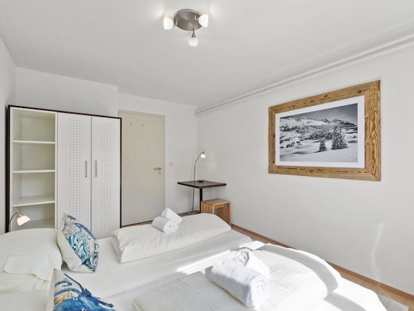 A bedroom with a bed, a wardrobe, a desk, and a framed picture on the wall.