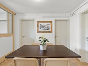 A dining area with a table, chairs, a potted plant, and a framed picture on the wall.