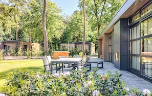 A modern outdoor patio with a dining table and chairs, surrounded by lush greenery and tall trees. - Nice home in Wenum-Wiesel with WiFi (Wenum-Wiesel)