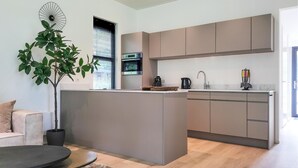 Et moderne køkken med en central ø, indbyggede hårde hvidevarer, samt et spiseområde med sofa og sofabord.