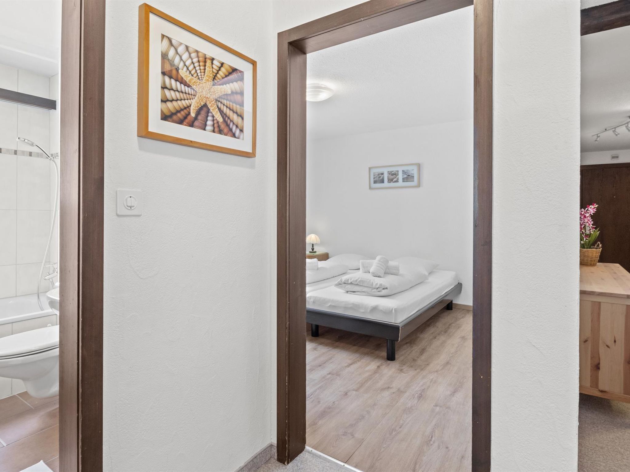 A hotel room with a bed, a bathroom with a shower, and a hallway leading to another room.