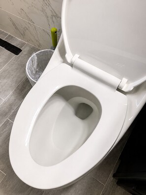 Een wit toilet met gesloten deksel in een badkamer met grijze betegelde vloer.