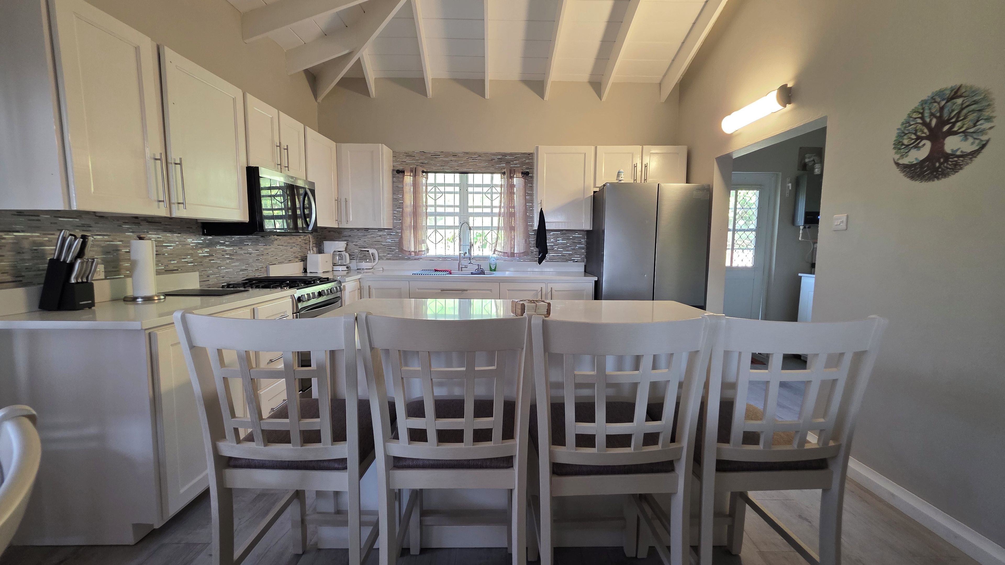 Una cocina moderna con armarios blancos, una isla central con sillas y vista al área de comedor.