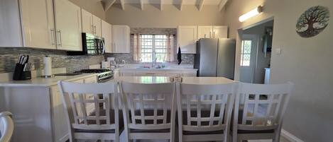 A modern kitchen with white cabinetry, a central island with chairs, and a view to the dining area.