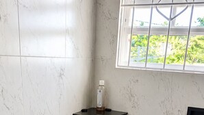 A bathroom with white marble tiles, a black shelf, and a window with a view of greenery. - Peaceful 3BR St. Kitts Mountain Getaway (Saint Peter)