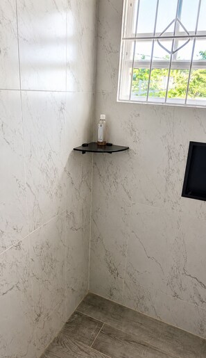 Un baño con azulejos de mármol blanco, un estante negro y una ventana con vistas a la vegetación.