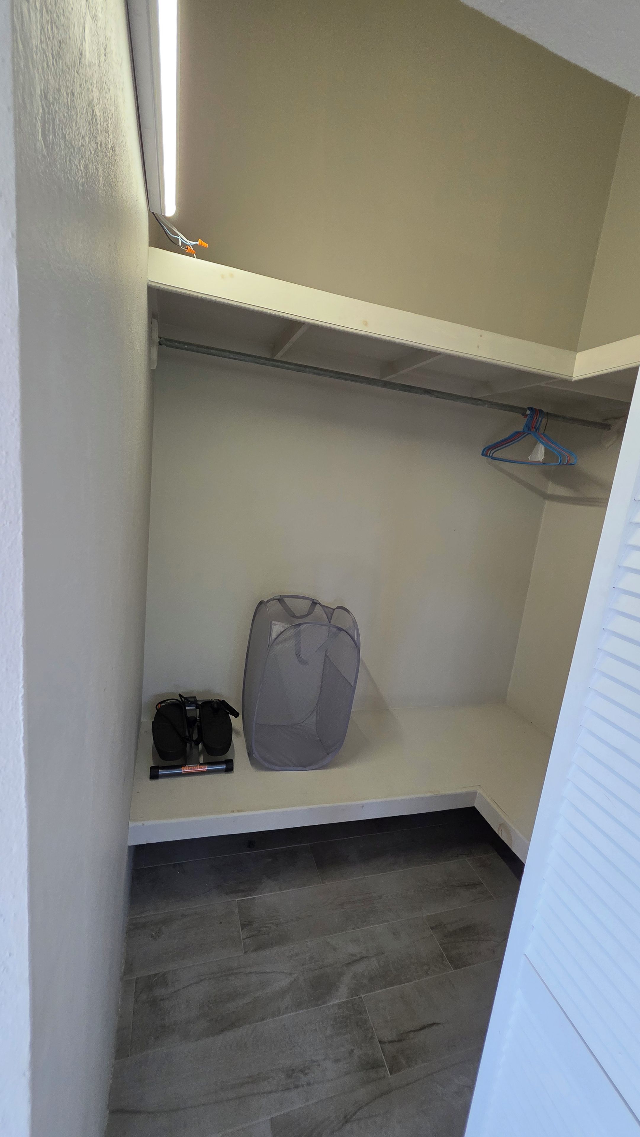 A closet with a hanging rod, a storage bench, and a pair of shoes.