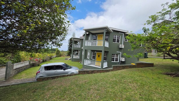 A two-story building with a balcony, a car parked in front, and a grassy area. - Peaceful 3BR St. Kitts Mountain Getaway (Saint Peter)