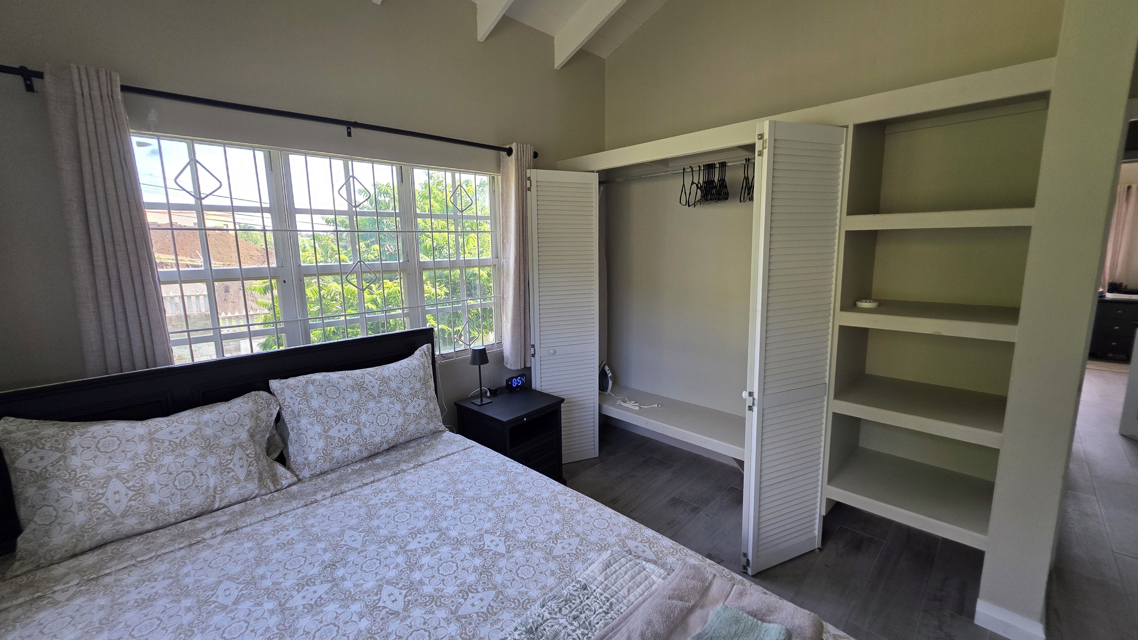 A bedroom with a bed, a bedside table, a window with curtains, and a wardrobe with shelves.