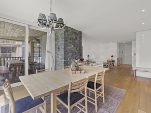 A modern dining area with a wooden table and chairs, a stone accent wall, and a glass door leading to an outdoor space. - Triangel Raber Appartement/Fewo Triangel Raber by Interhome (Parpan)