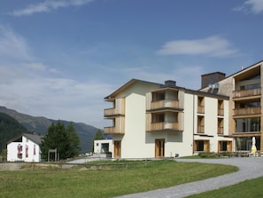 A multi-story building with balconies, a gravel path, and a mountainous backdrop. - Triangel Raber Appartement/Fewo Triangel Raber by Interhome (Parpan)