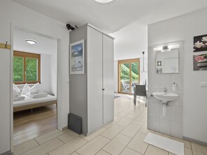 Ein modernes Hotelzimmer mit Bett, Schrank, Badezimmer mit Waschbecken und Blick auf Grünflächen.