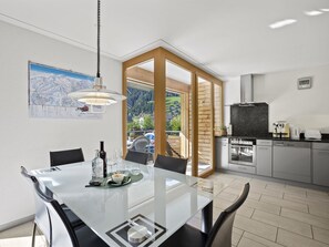 A modern kitchen with stainless steel appliances, a dining area with a glass table, and a view of a mountainous landscape through large windows. - Hemmadi Appartement/Fewo,   Ferienwohnung Hemmadi by Interhome (Churwalden)