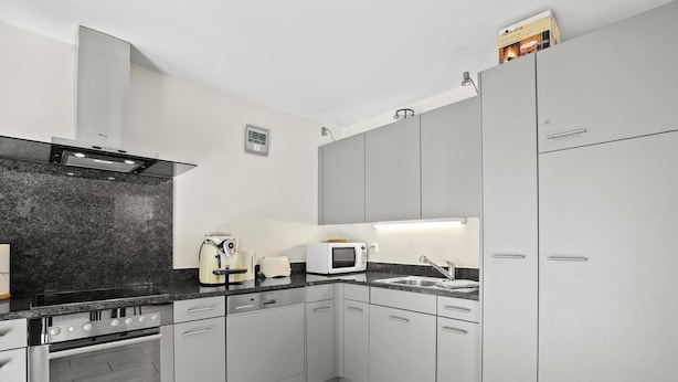 Eine moderne Küche mit grauen Schränken, einem eingebauten Backofen, einer Mikrowelle und einer Kaffeemaschine.